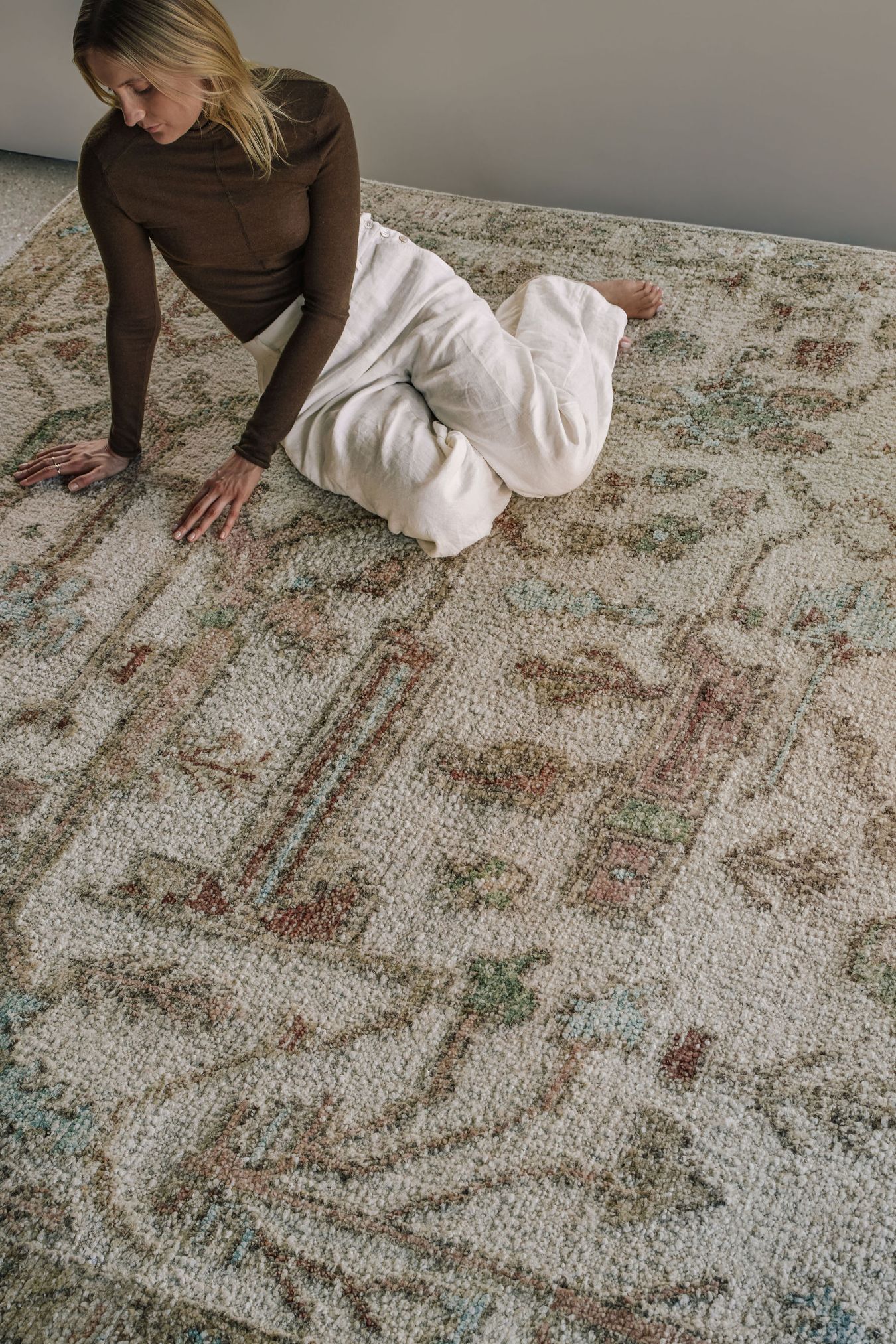 Close-up of the Biraz rug from the Oushak Collection, featuring a traditional pattern in cream, olive, terracotta and turquoise beneath a tan leather chair.