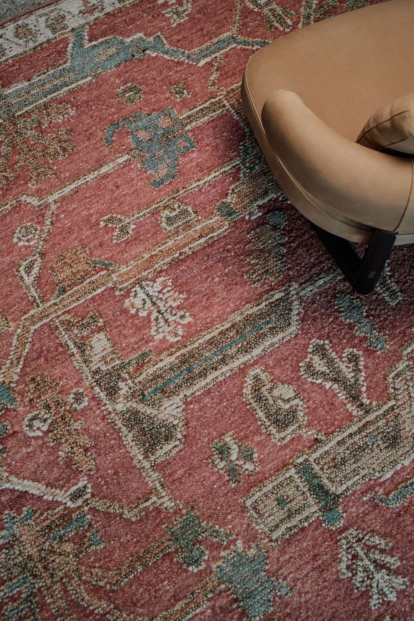 Close-up of the Biri rug from the Oushak Collection, featuring a red, cream and muted blue traditional pattern beside a tan leather chair.