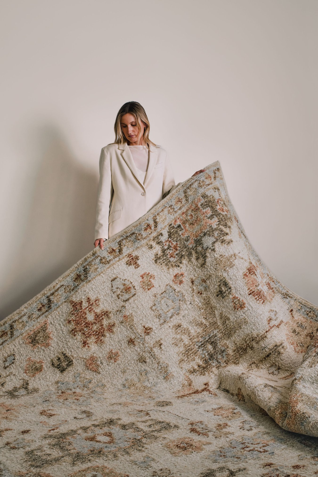 Woman in a white suit holding the Hemen rug from the Oushak Collection, featuring a traditional pattern in cream, soft blue, olive and terracotta.