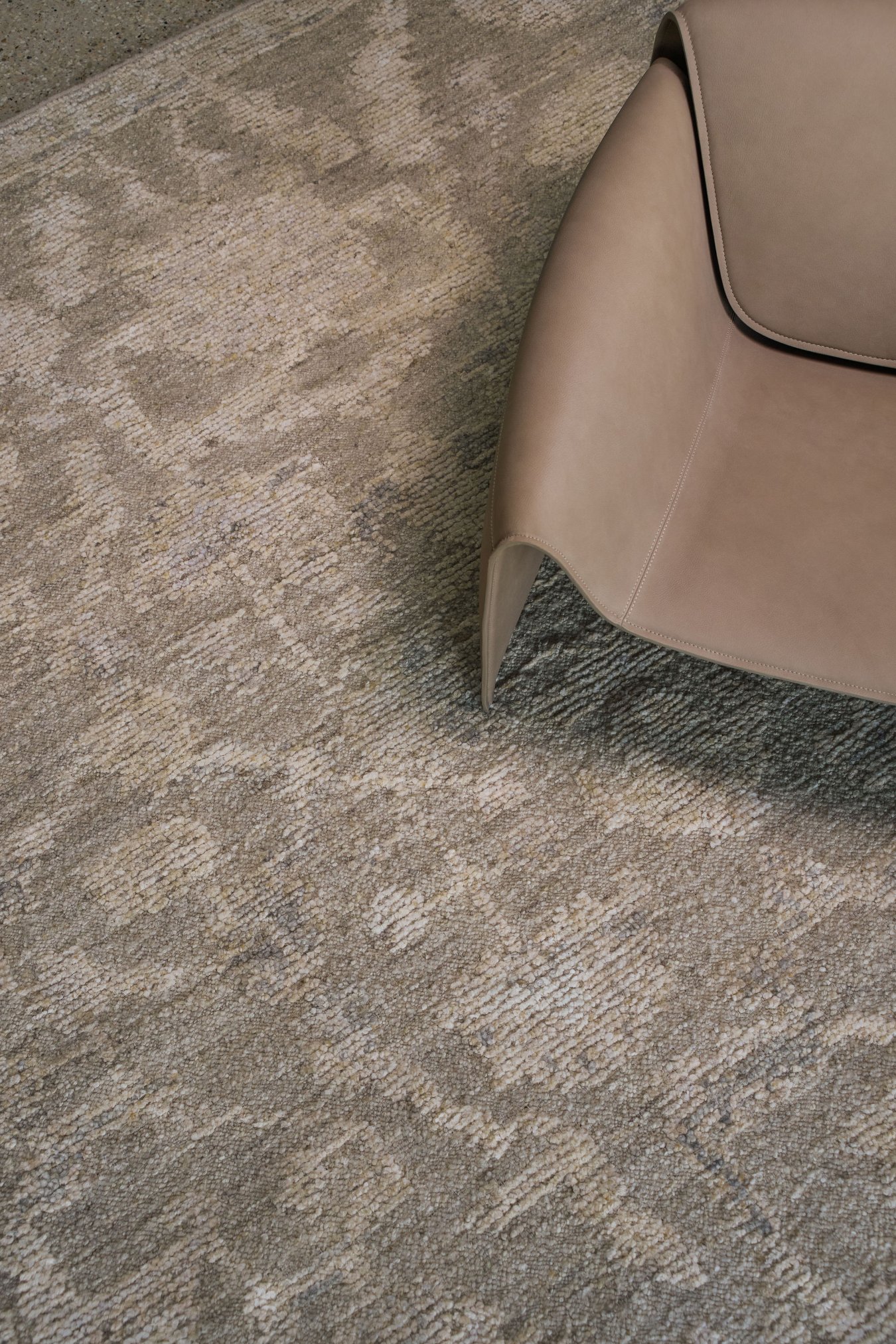Close-up of the Olarak rug from the Oushak Collection, featuring a textured taupe, grey and cream pattern beside a soft brown leather chai