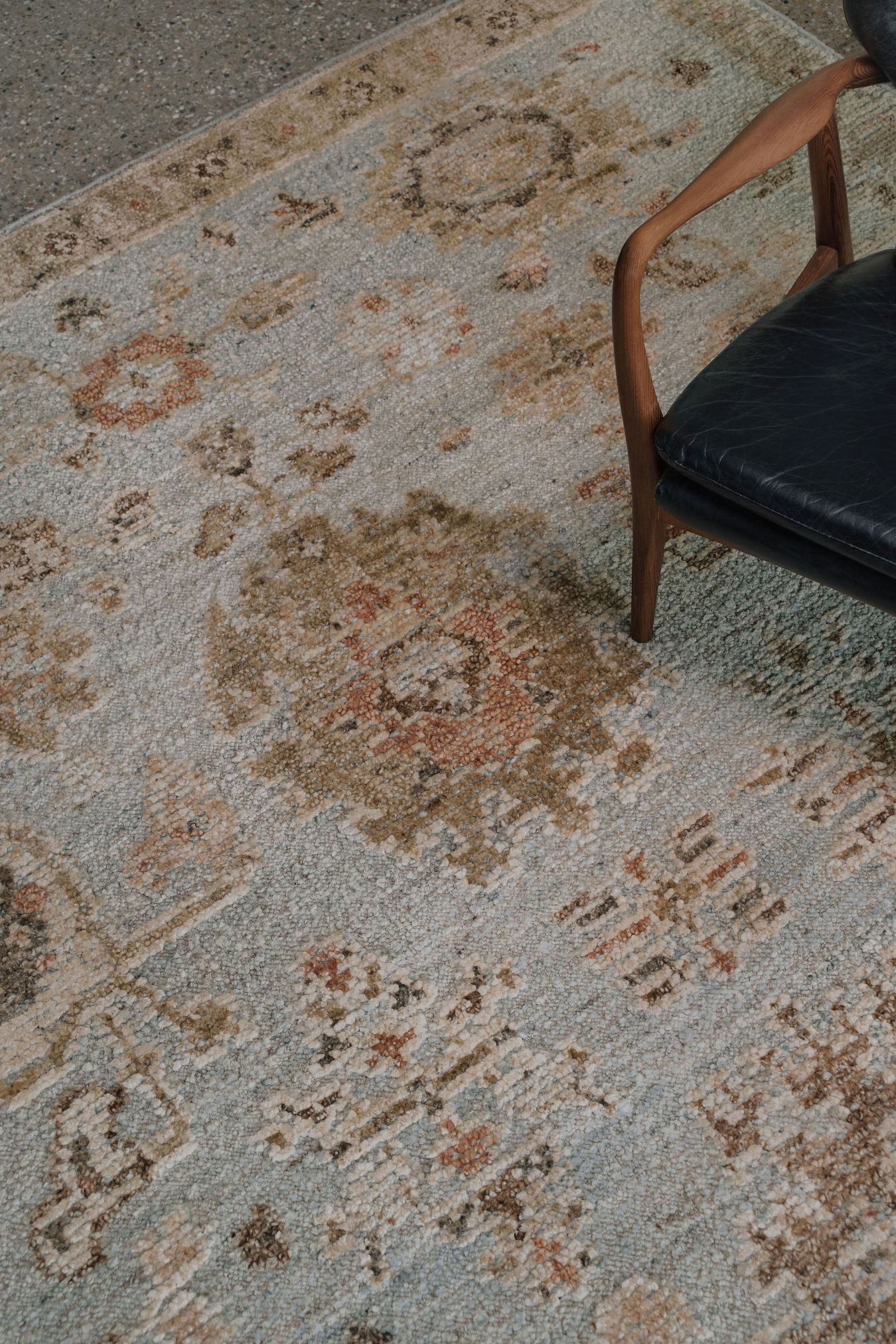 Close-up of the Yok Blue rug from the Oushak Collection, featuring a soft blue, beige and terracotta traditional pattern beside a timber and black leather chair.